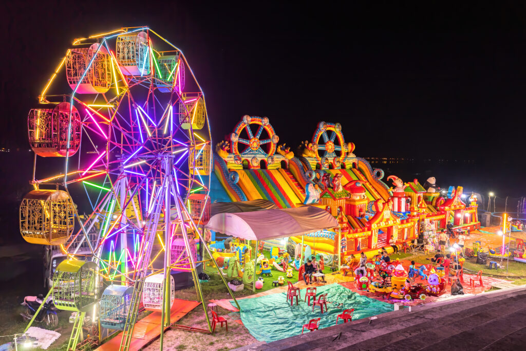 Illuminated_Ferris_wheel,_bouncing_castle_and_carousel_at_night_in_a_funfair_in_Vientiane,_Laos